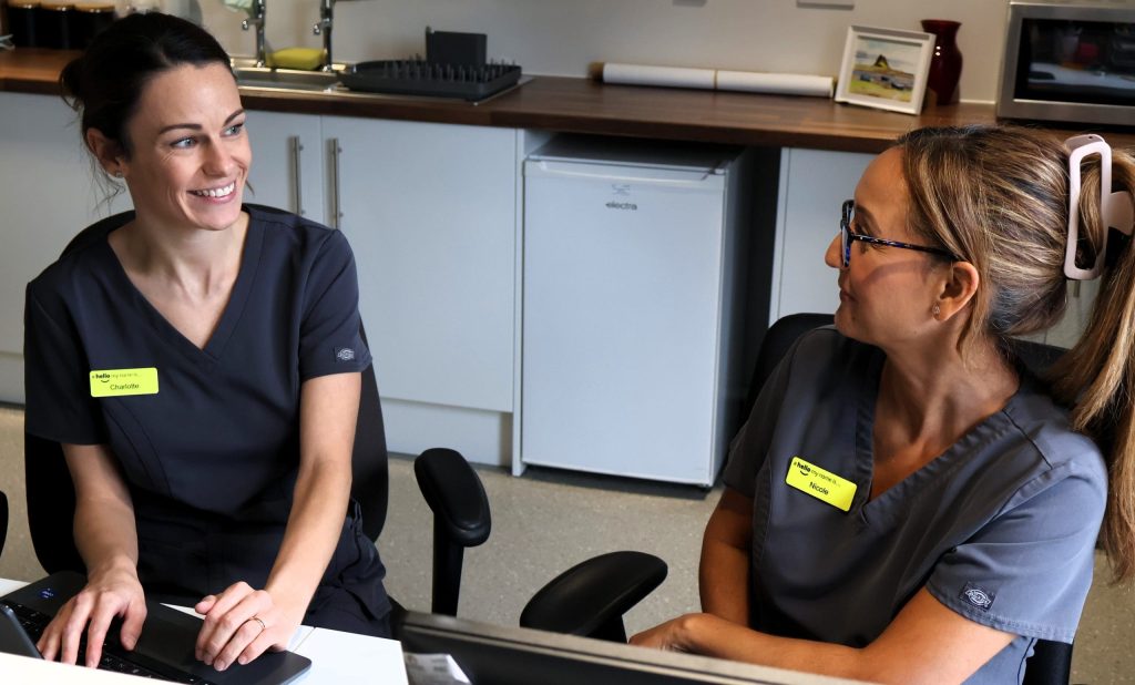 Our physiotherapists, Charlotte and Nicole, sat behind their desks looking towards each other and smiling
