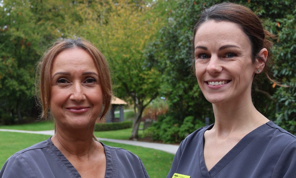 Nicole and Charlotte, our Physiotherapy team, in the Compton Hall gardens wearing grey uniforms and smiling at the camera